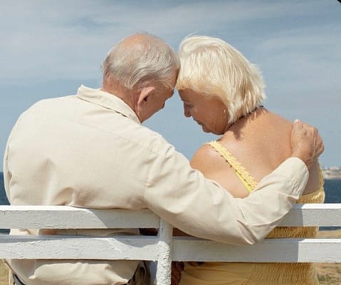 An elderly couple seated on a bench overlooking the water