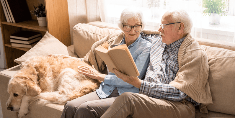 Elderly couple reading together on a sofa with a dog