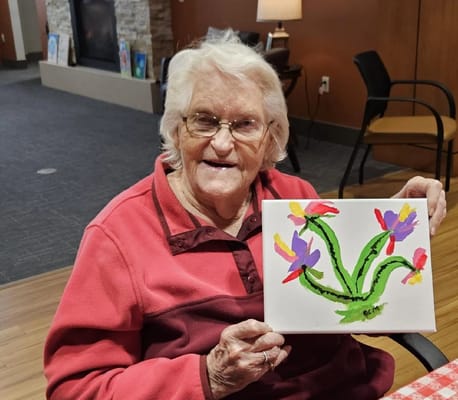 A smiling resident holding a painted flower artwork