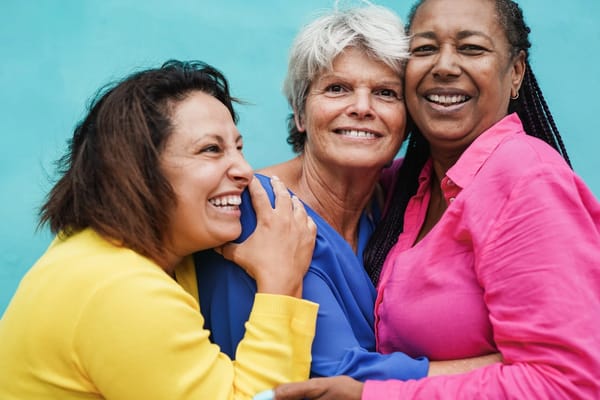 Three women smiling and embracing outdoors