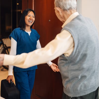 A caregiver welcoming a senior resident at their door