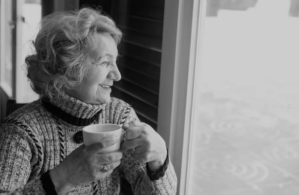 Elderly woman enjoying a hot drink while gazing out the window.