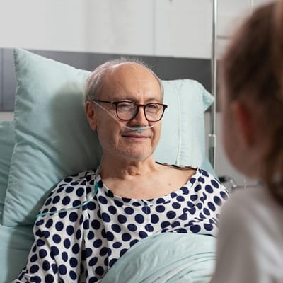 A senior man in a hospital bed smiling at a visitor