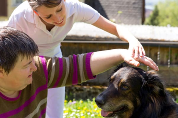 A resident interacting with a dog and staff outside