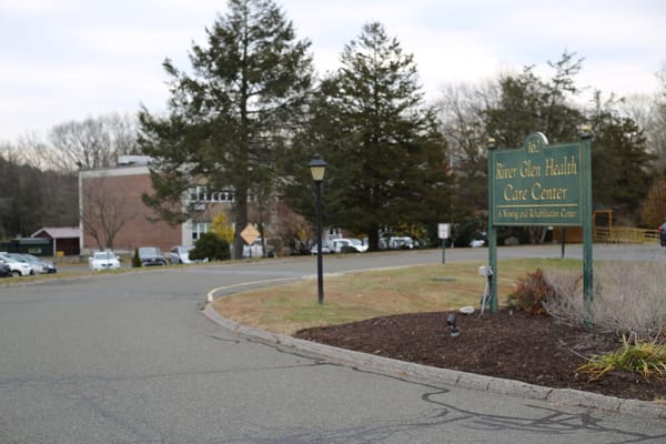 Entrance sign of River Glen Health Care Center with a road leading in