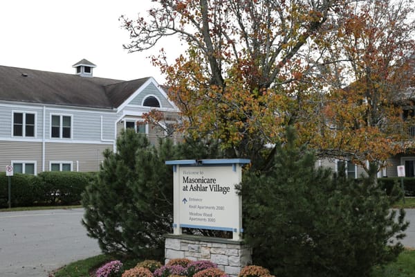 Welcome sign for Masonicare At Ashlar Village, surrounded by trees