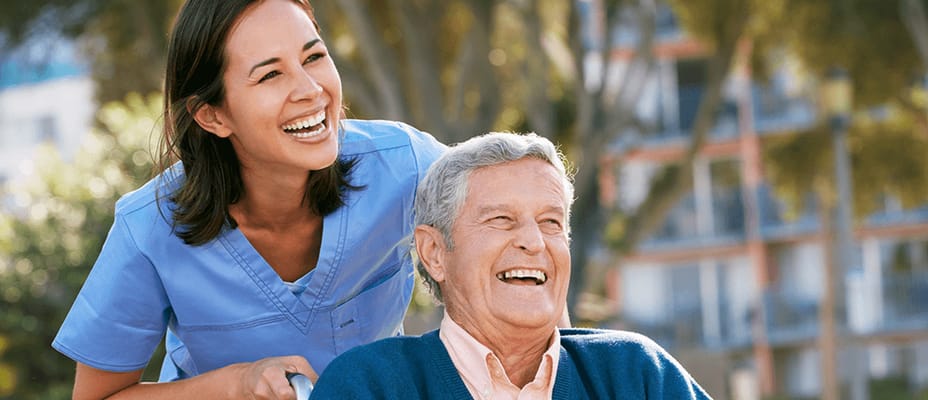 A caregiver and elderly resident enjoying laughter outdoors.