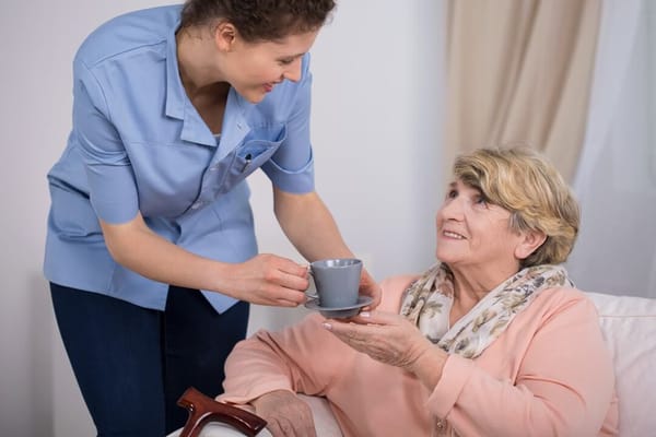 Caregiver serving hot drink to smiling senior