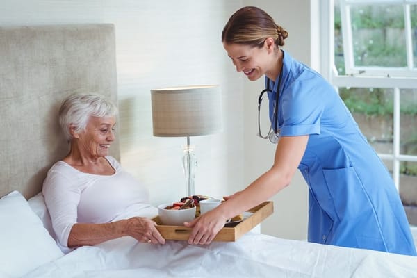 Nurse serving food to a smiling resident in bed