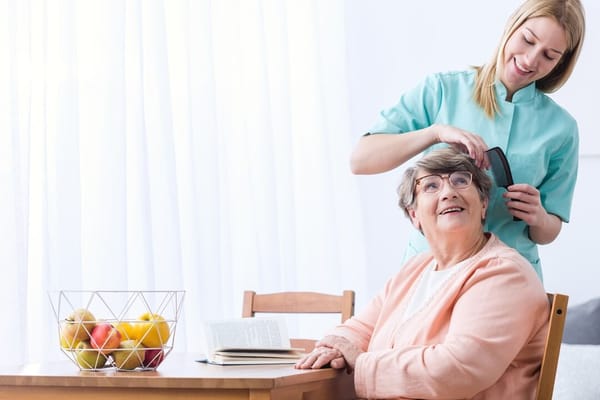 Caregiver styling an elder's hair in a bright room
