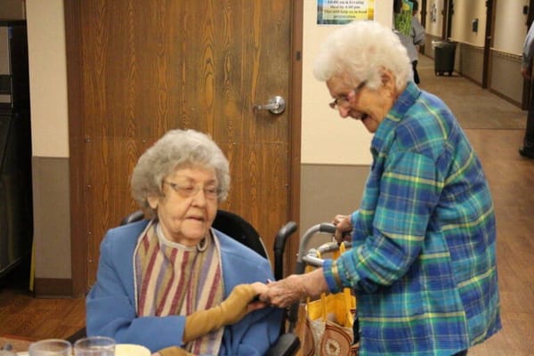 Two elderly women interacting in a cozy common area