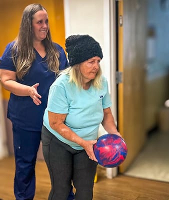 Resident participating in a bowling activity with staff assistance