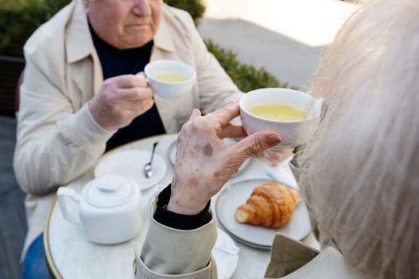 Two seniors enjoying tea and croissants outdoors