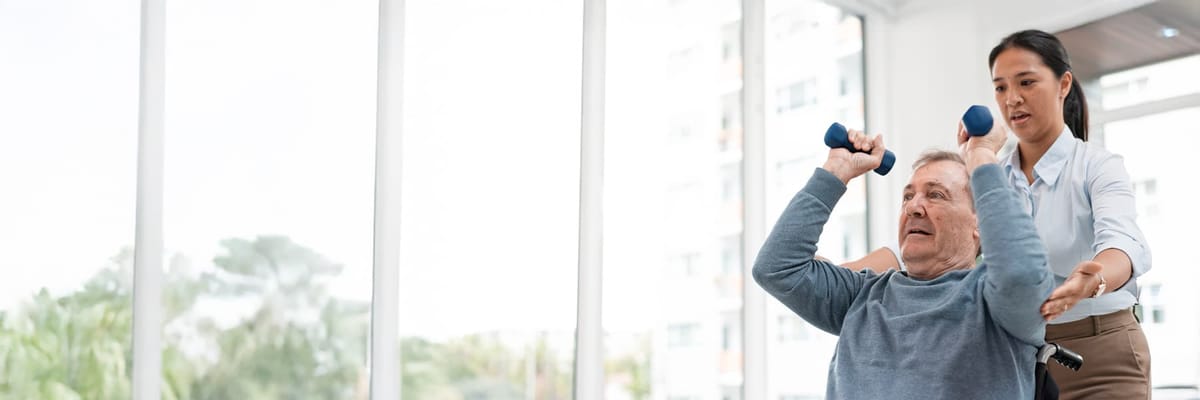 A staff member assisting a resident with weights in a bright room
