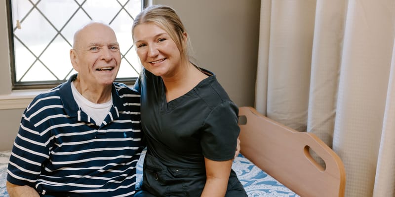 A resident and staff member smiling together in a room