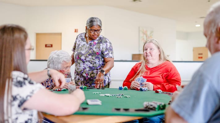 Residents participating in a card game with staff assistance
