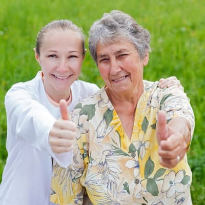 Senior resident and caregiver smiling with thumbs up
