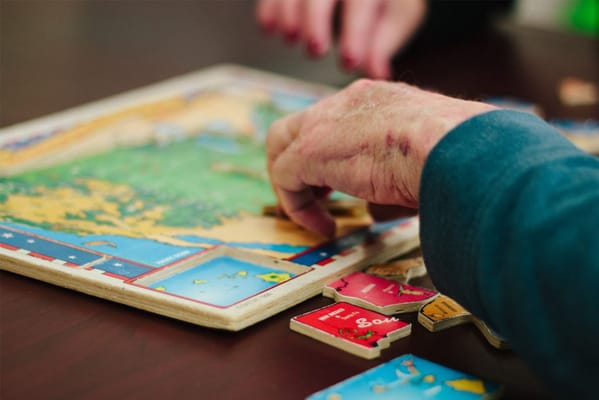 A senior's hand placing puzzle pieces on a table