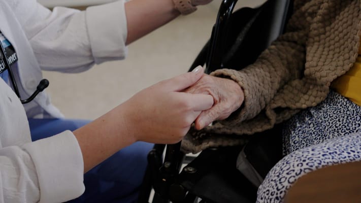 A caregiver holding a senior's hand in a facility