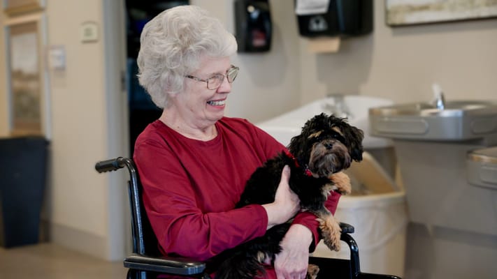Senior woman holding a small dog in a facility.