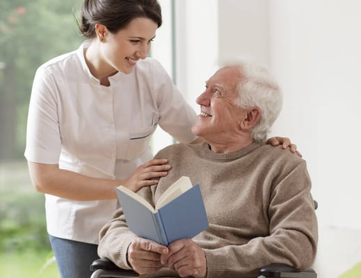 Caregiver reading to a smiling elderly man