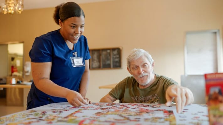 A caregiver assisting a resident with a puzzle indoors