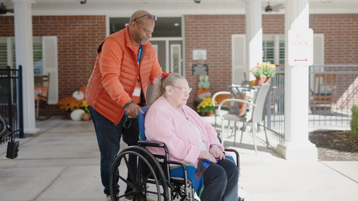 A caregiver assisting a resident in a wheelchair outdoors