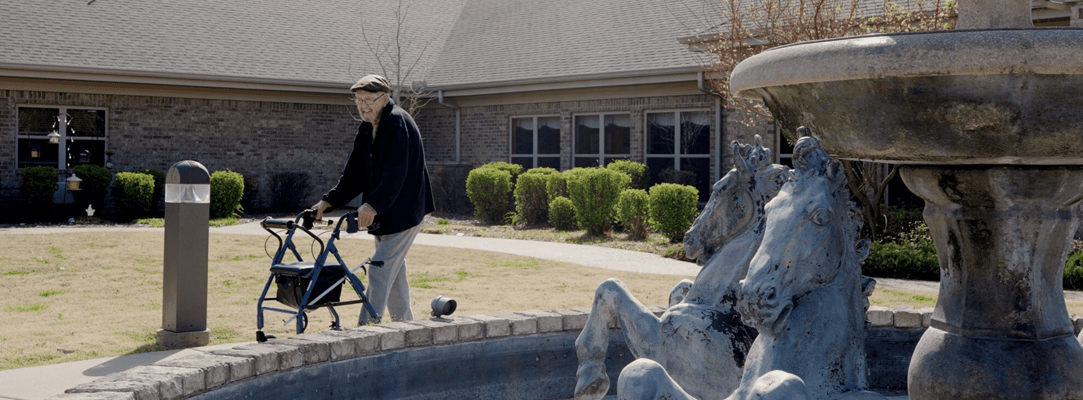 Resident using a walker near a fountain in the garden