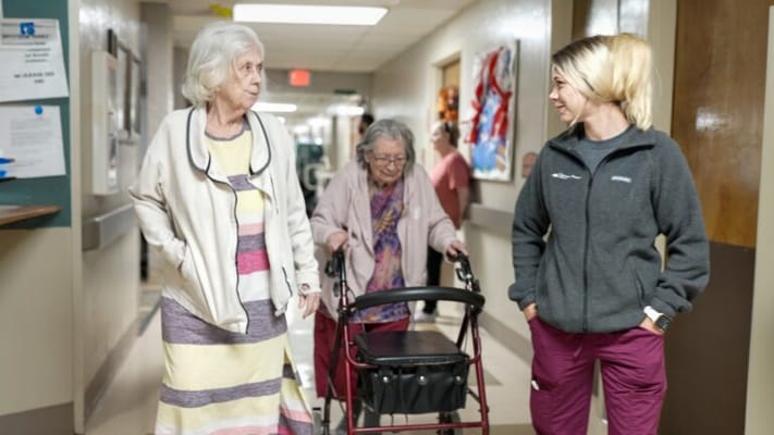 Residents walking with staff in a facility hallway
