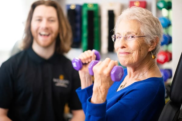 Senior woman exercising with dumbbells alongside a staff member