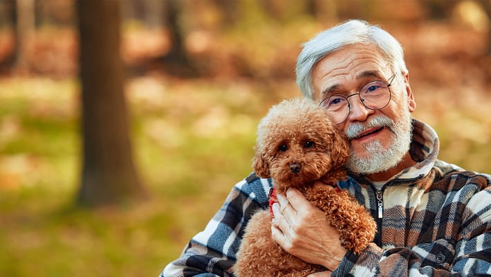 Senior man smiling while holding a small dog outdoors