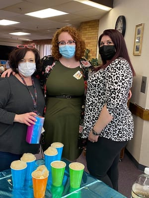 Staff members posing with colorful cups in an activity room