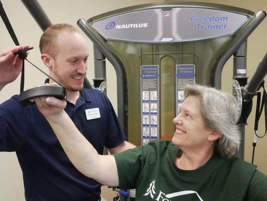 Resident exercising with staff assistance in a gym