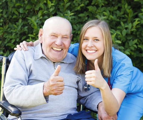 Smiling senior man and healthcare worker giving thumbs up outdoors
