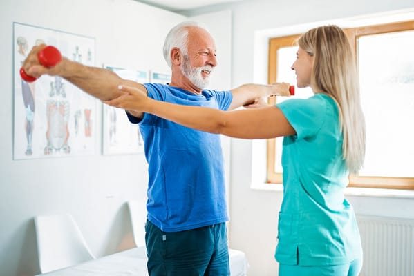A senior man exercising with assistance in a therapy room