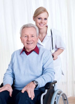 A nurse assisting a smiling elderly man in a wheelchair