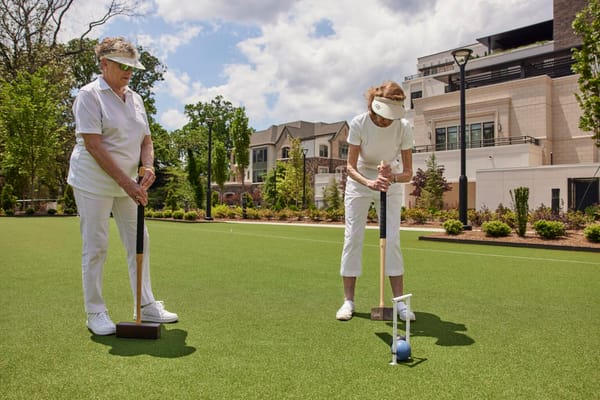 Residents playing croquet on a green lawn