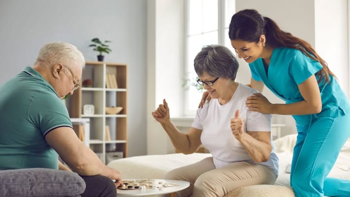 Residents playing a board game with staff in a bright room