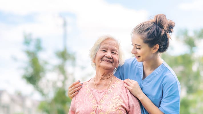 A caregiver smiling with a senior resident outdoors