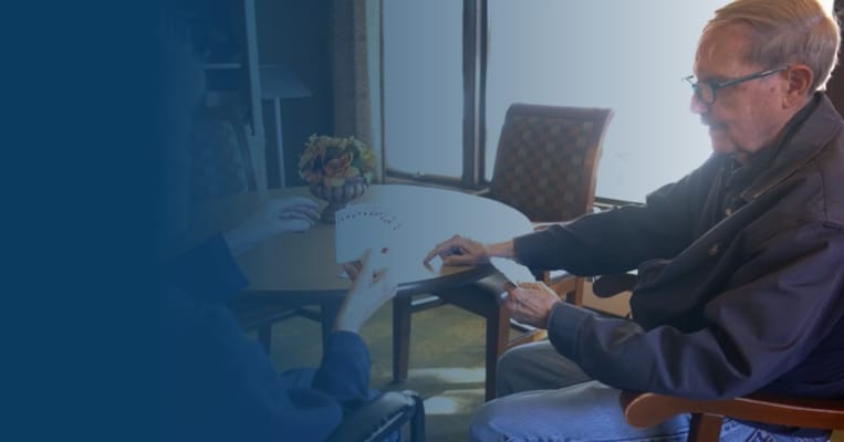 Two seniors playing cards at a table in a bright room