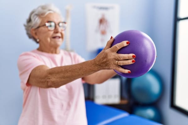 Senior woman exercising with a purple ball in a therapy room