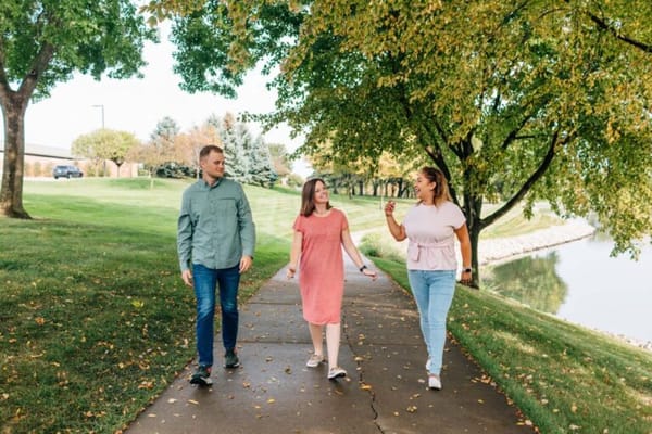 Three people walking along a path by a pond