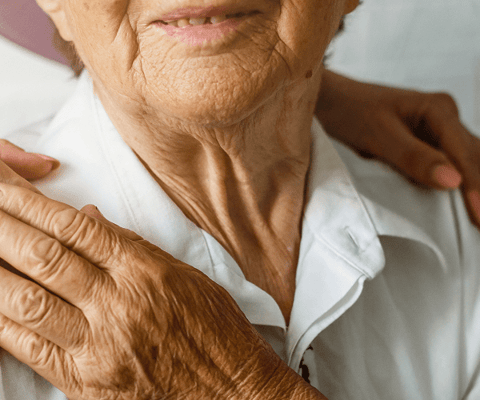 Close-up of a senior's smiling face with a caregiver's hand