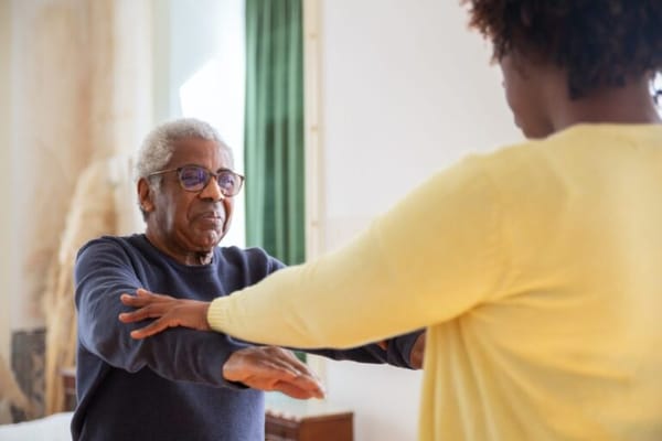 Senior resident participating in a balance exercise with staff assistance
