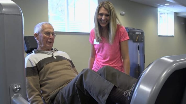 Senior man exercising with a staff member in a gym