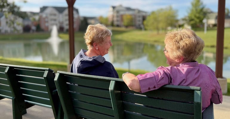 Two women chatting on a bench by a pond