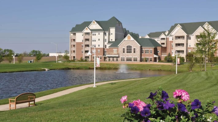 Exterior view of a senior living facility with a pond and flowers