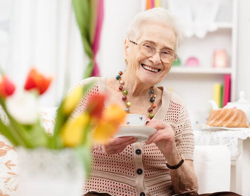 Smiling elderly woman holding a teacup in a cozy room