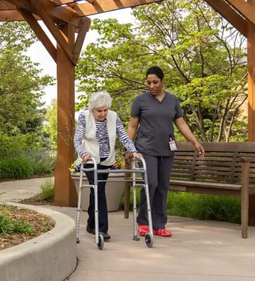 Elderly resident using a walker with staff assistance