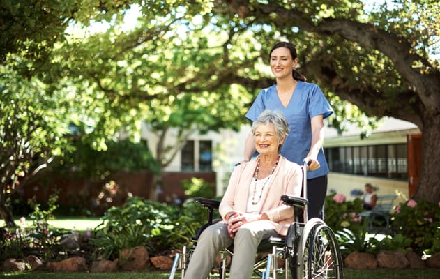 A caregiver assisting a smiling resident in a garden
